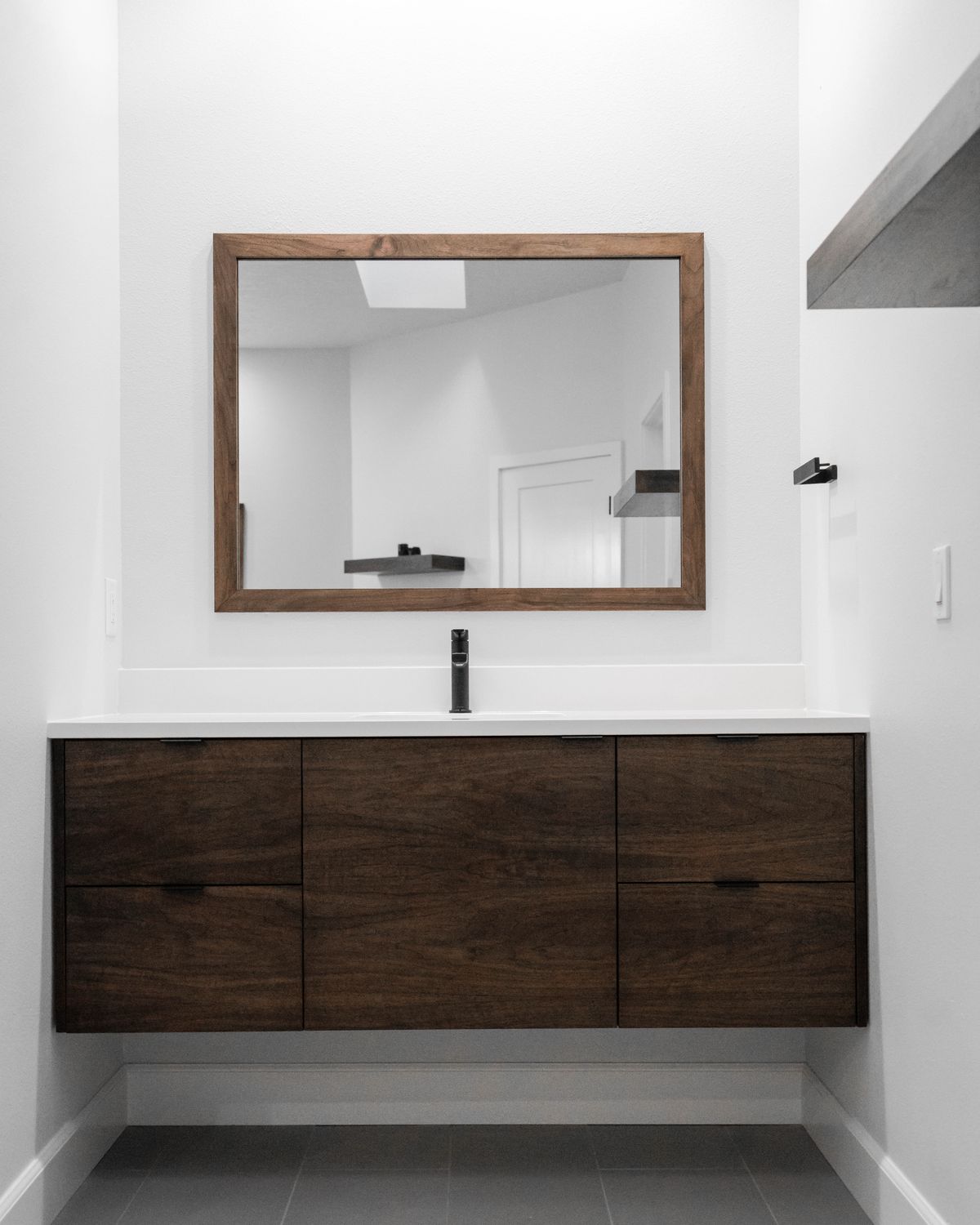 Custom floating walnut vanity with a black faucet and walnut-framed mirror