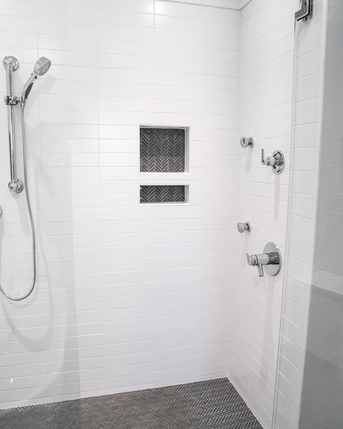 Shower with a herringbone tile floor and stacked niche