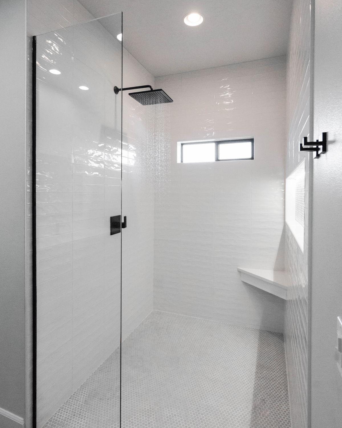 Walk-in shower with a matte black rain head, penny tile floor, and corner bench
