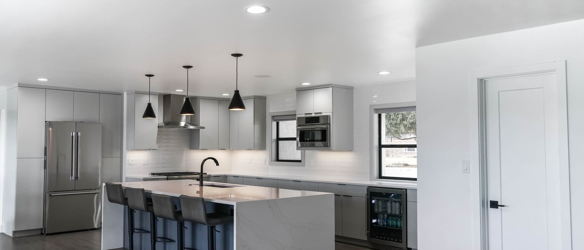 Kitchen remodeled by DH Homes with grey flat-panel cabinets, a white quartz waterfall island, and black pendant lights