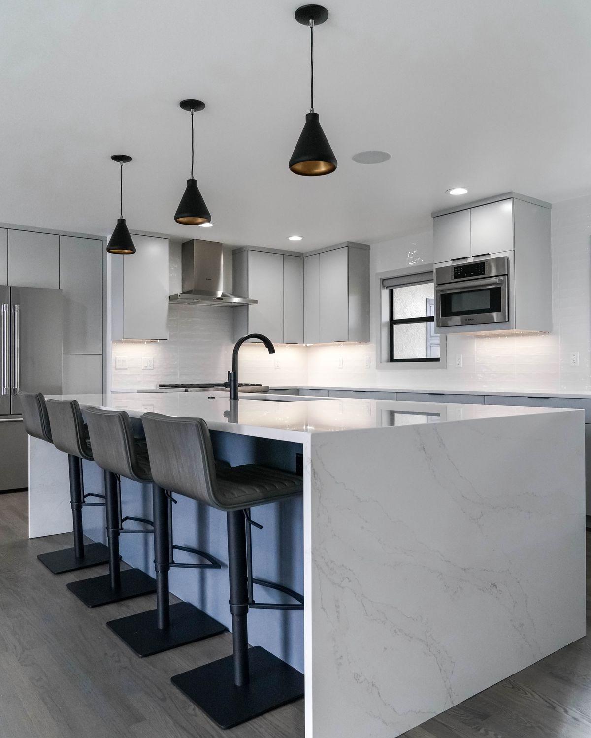 Grey flat-panel kitchen island with four bar stools and black cone pendants