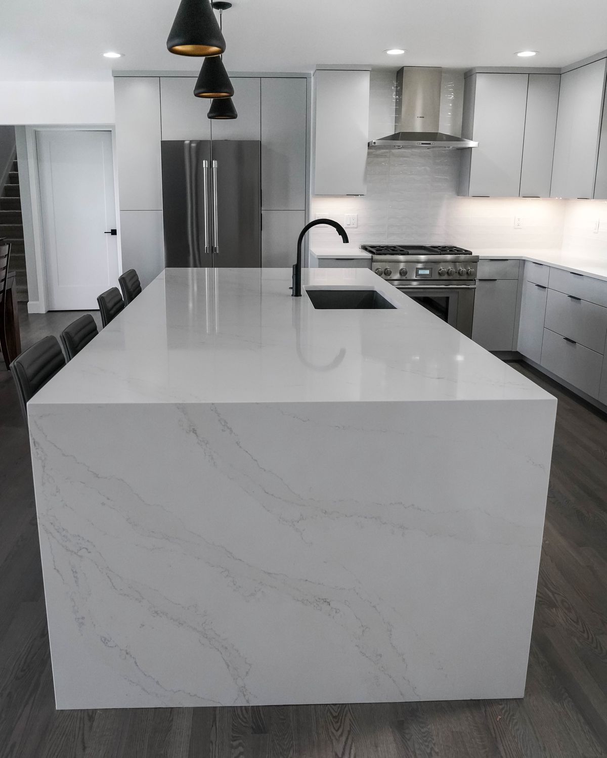 Waterfall quartz island end with a grey kitchen behind it