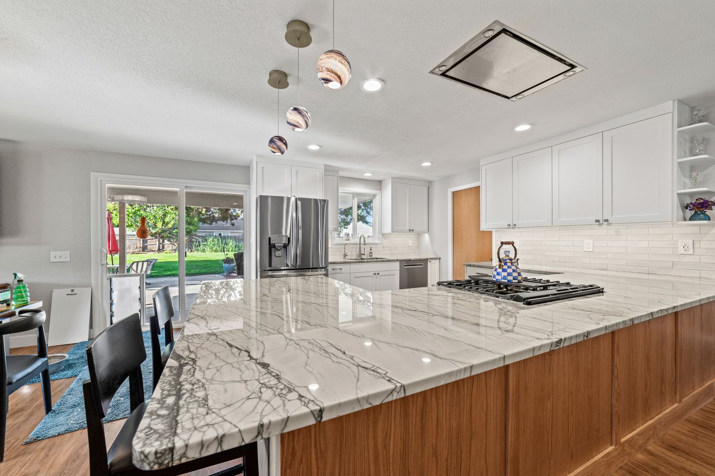 White shaker kitchen remodel with a quartzite peninsula, gas cooktop, and glass pendants
