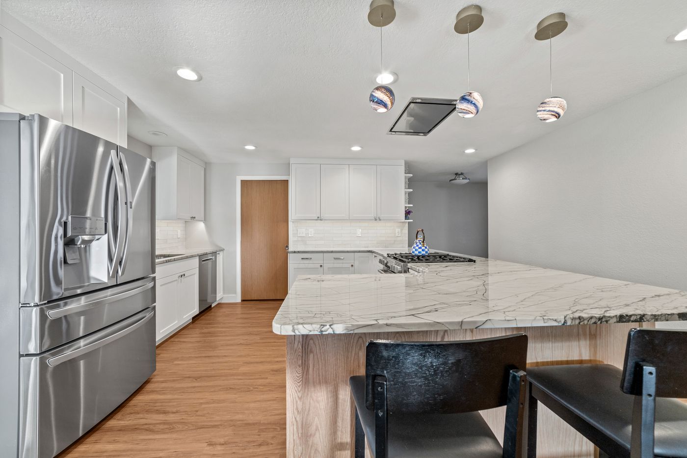 White shaker kitchen with a quartzite peninsula and glass pendants